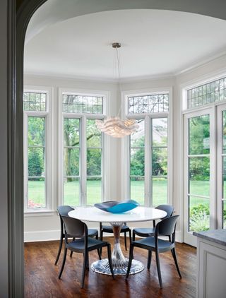 breakfast nook with white round table in bay window with contemporary feather light fitting