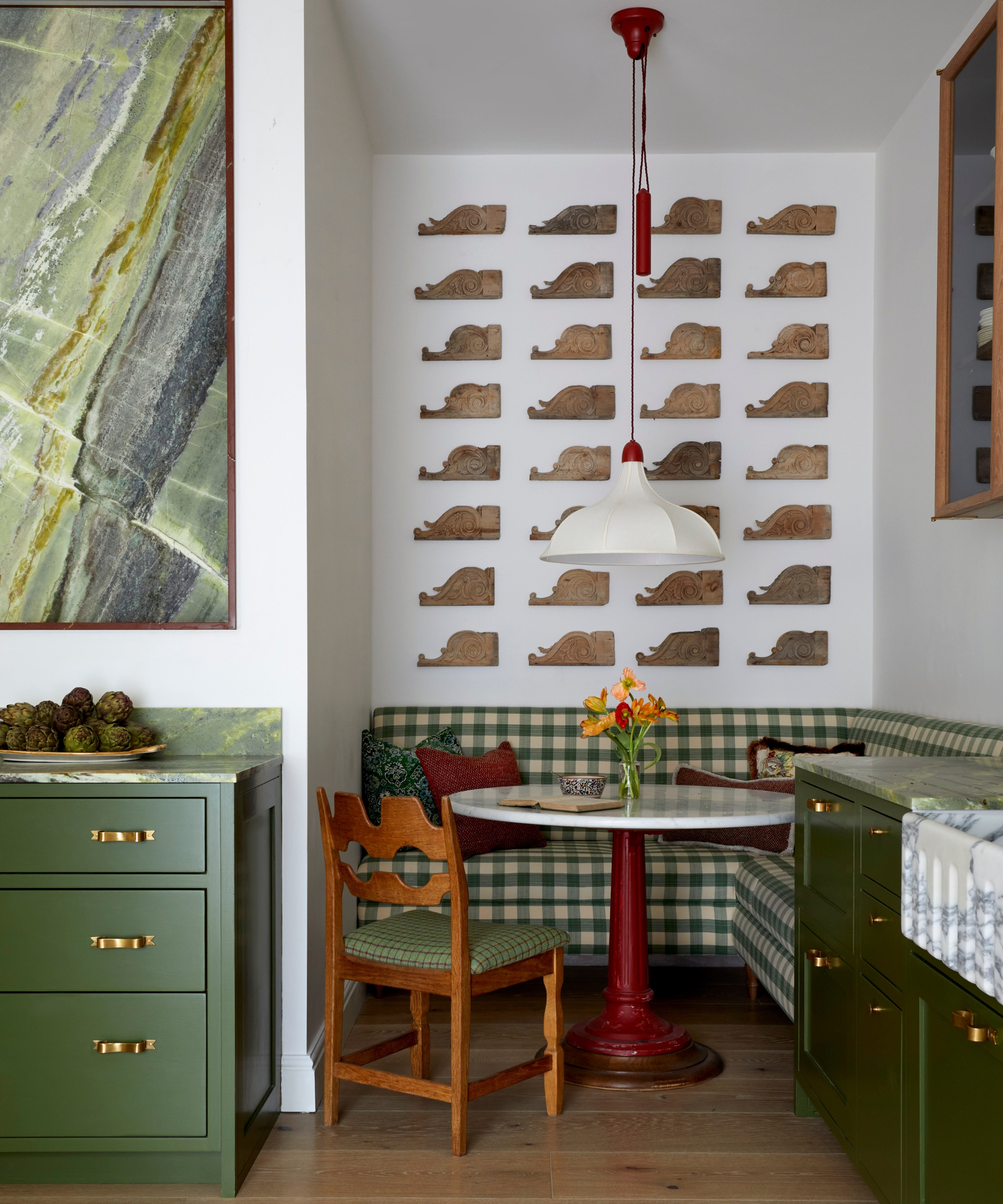A charming dinette in a kitchen alcove featuring green and white gingham upholstery, a round marble table on a wood pedestal, and wooden chairs with matching upholstery to the banquette