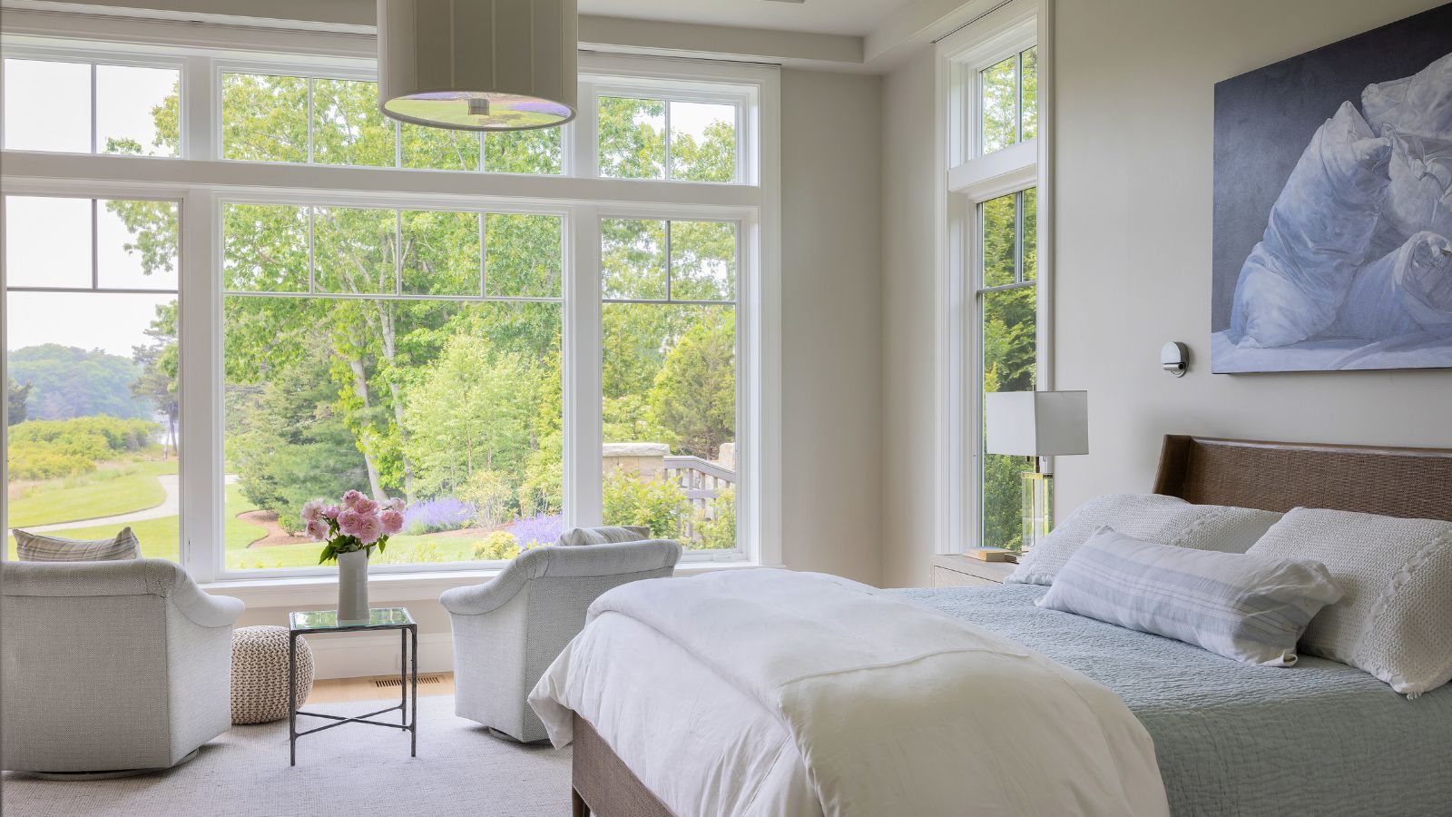 Light bedroom with garden view through large windows, and living area with two armchairs facing out 