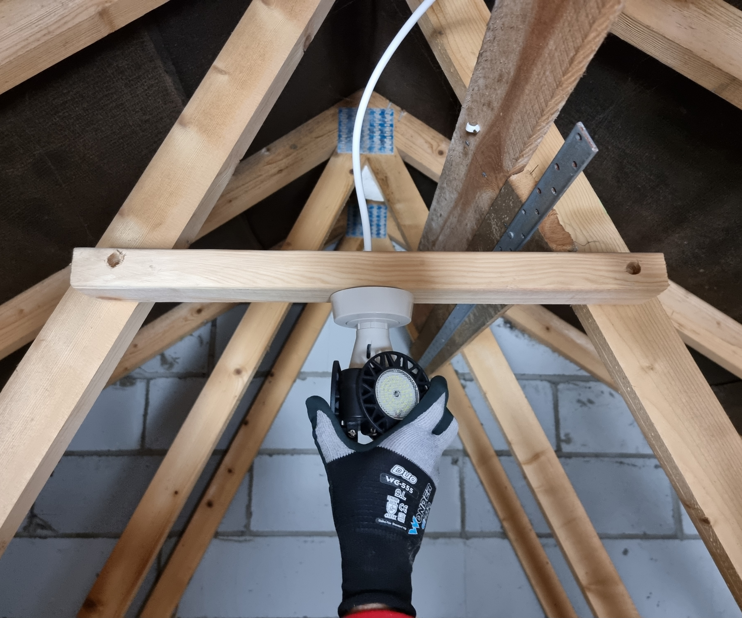 hand holding light fitting attached to roof trusses in loft