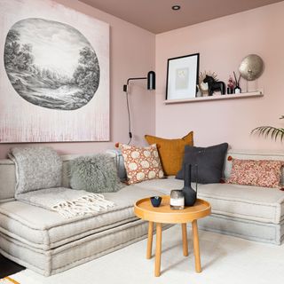 A pink living room with a corner sofa and wooden table