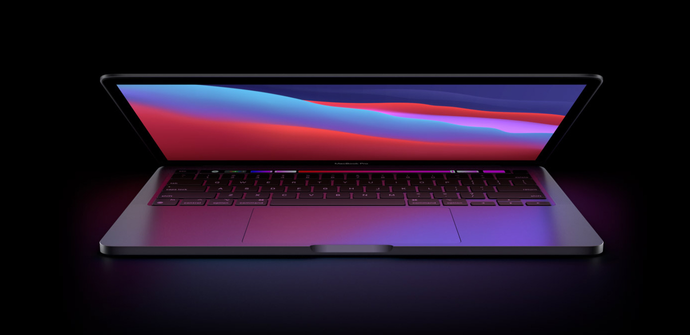 A half-opened MacBook Pro 2020 on a dark desk against a dark background. The screen shows a typical Apple desktop background