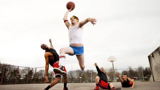 A man dunking over three old men on a basketball court.