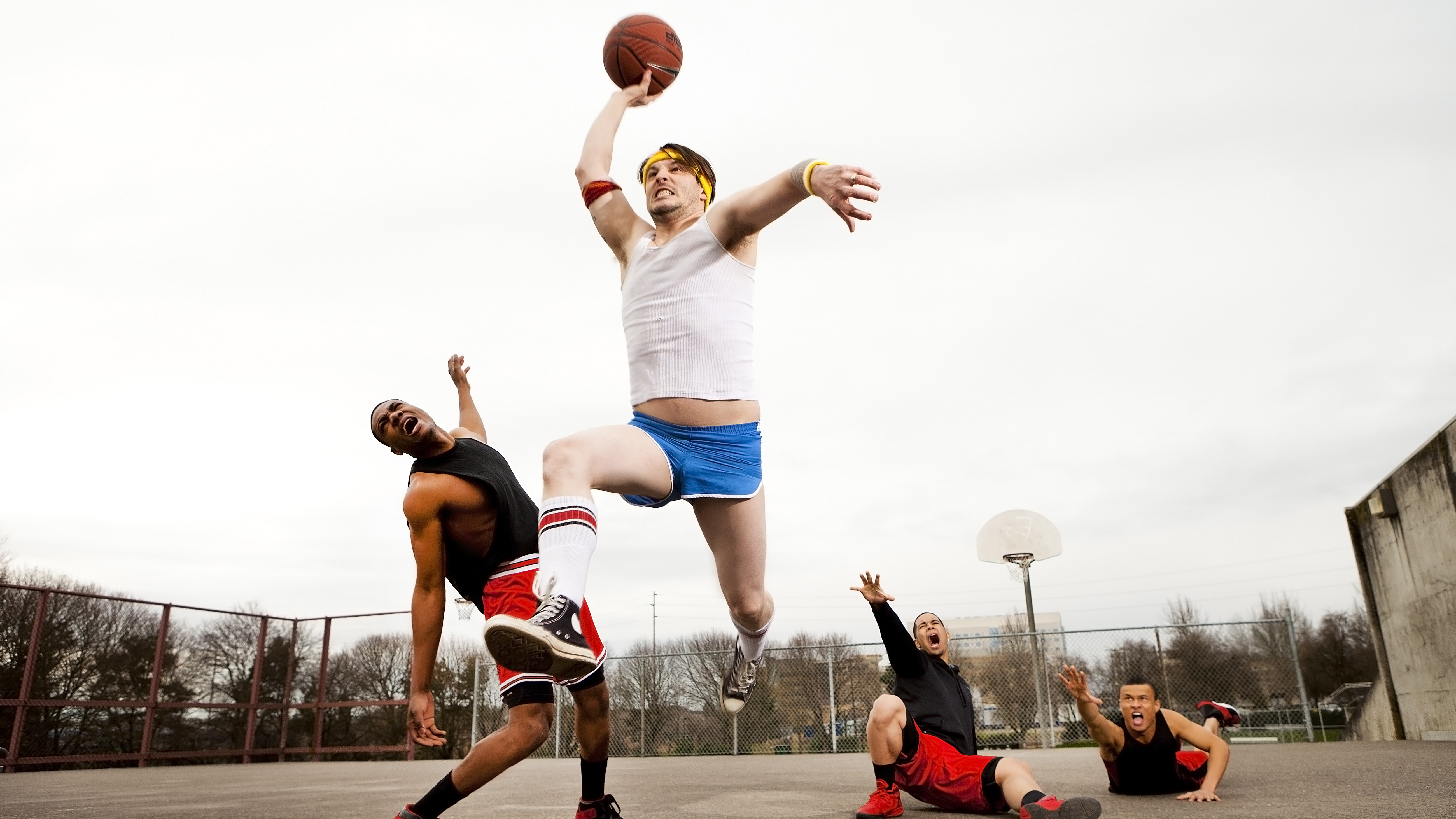 A man dunking over three old men on a basketball court.