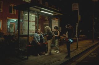 jessica gunning has her makeup done while sitting at a bus stop at night, as members of the production crew stand nearby, while filming the netflix series 'baby reindeer'