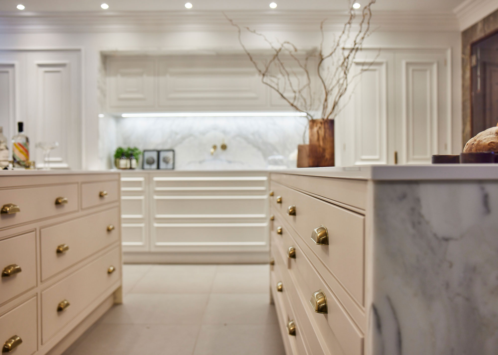 white kitchen with marble waterfall work surface and brass cabinet handles