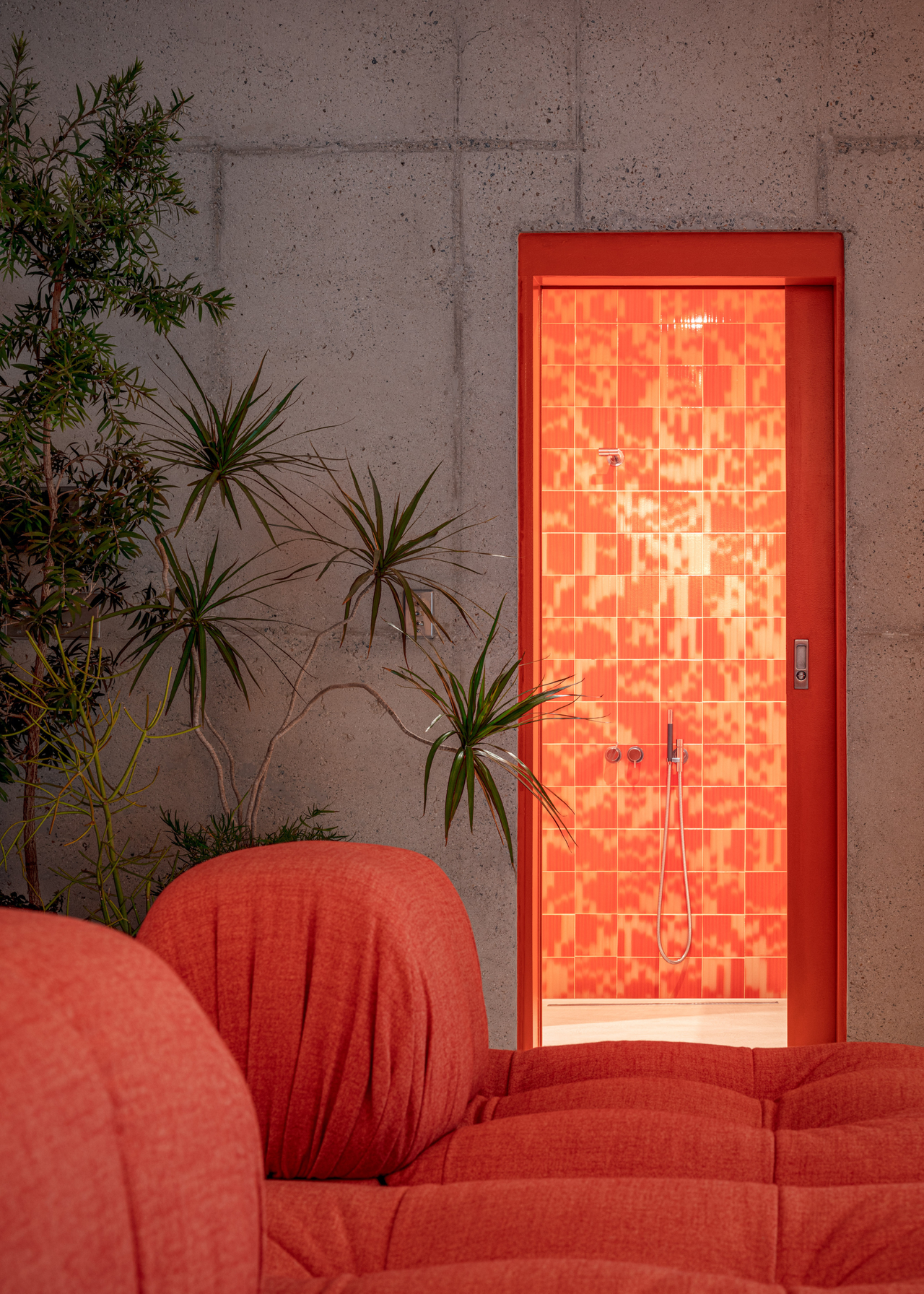 concrete walls with an orange doorway leads to a bathroom with orange and red palet tiles