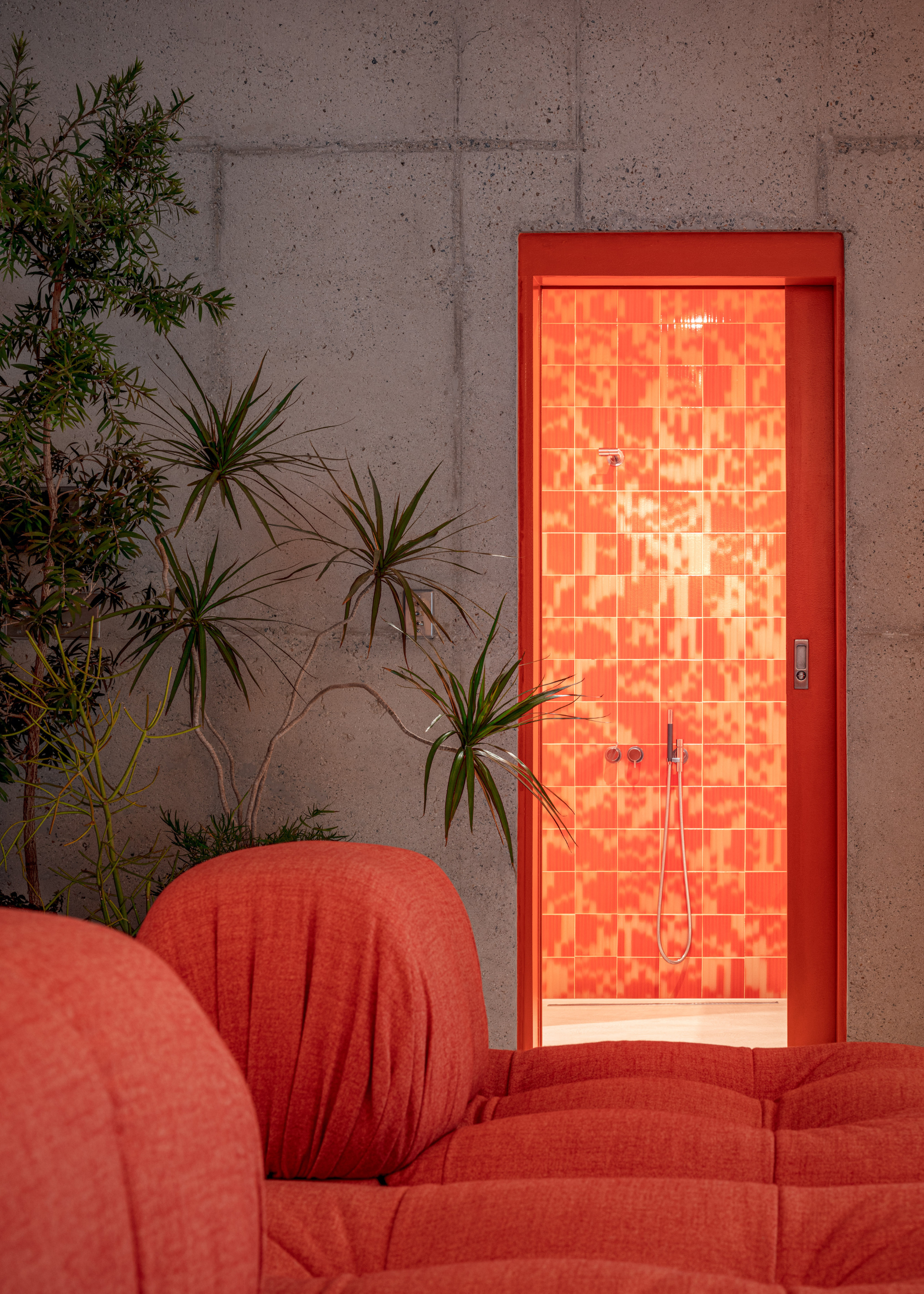 concrete walls with an orange doorway leads to a bathroom with orange and red palet tiles