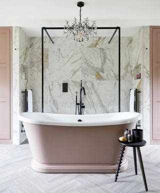 Small bathroom with large scale marble-effect tiles and freestanding tub with pink exterior with chandelier above