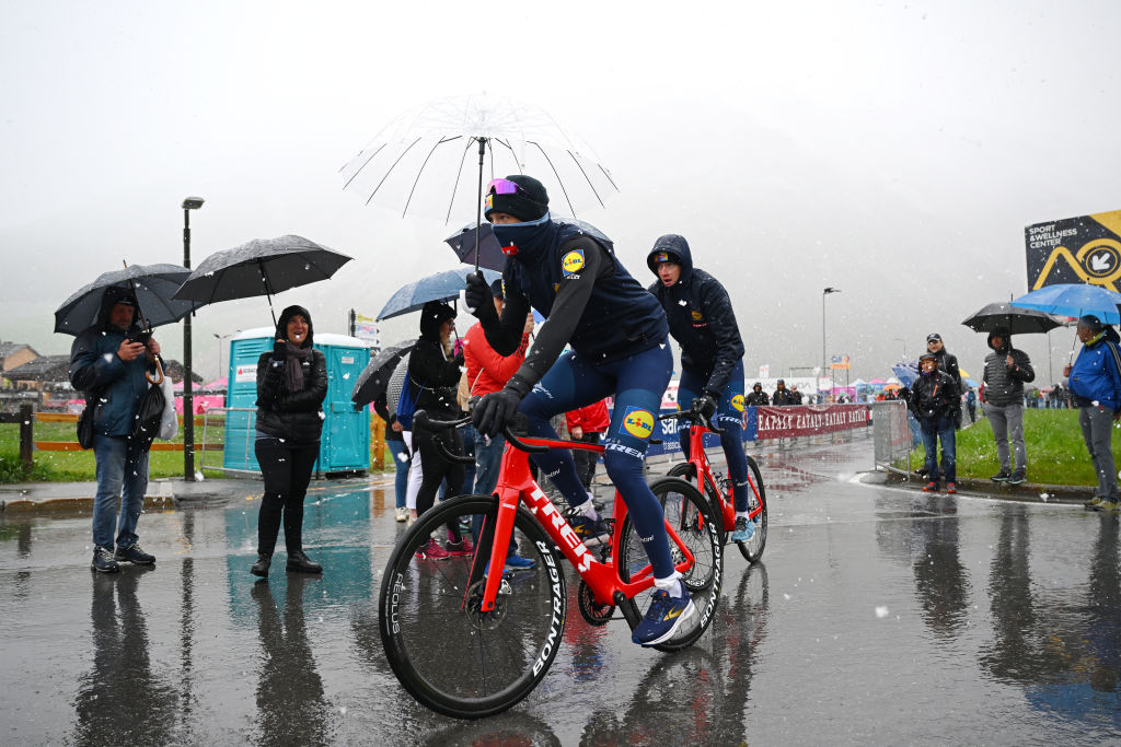 Jonathan Milan rides to the start of a Giro d'Italia stage holding an umbrella and wrapped up warm as it snows