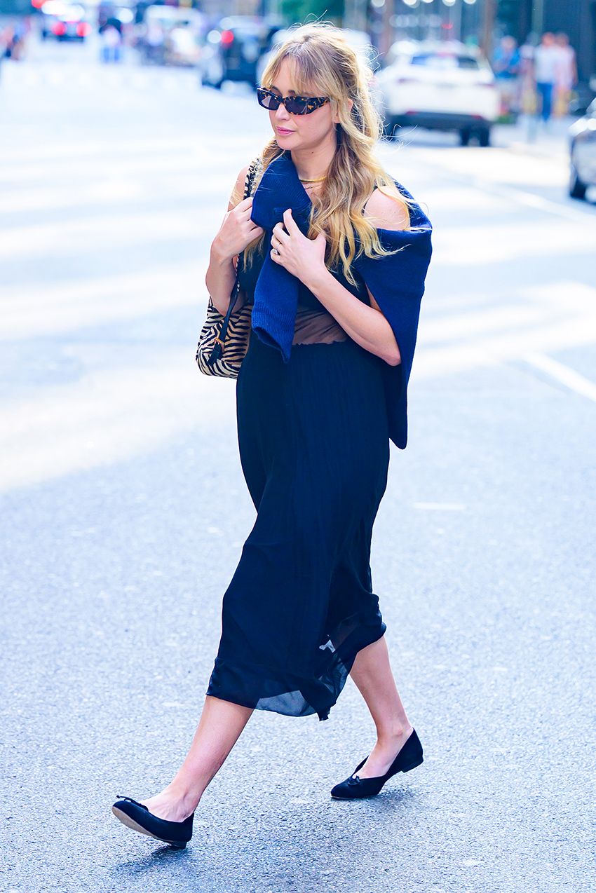 Jennifer Lawrence wearing a sweater around her shoulders, a midi dress, ballet flats, a mini backpack, and sunglasses