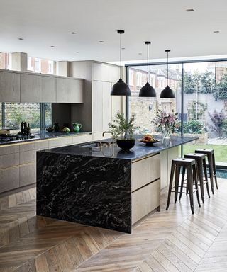 An example of kitchen extension ideas showing a kitchen with parquet flooring and an black marble island with metal bar stools and pendant lighting