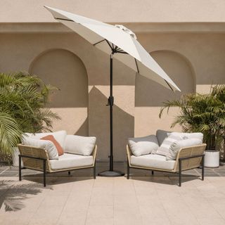 cream tilting patio umbrella in between two outdoor chairs