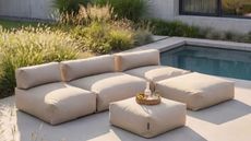 Image of a plush, modern outdoor sectional sofa on a pool deck in front of a pool and a few grassy bushes.