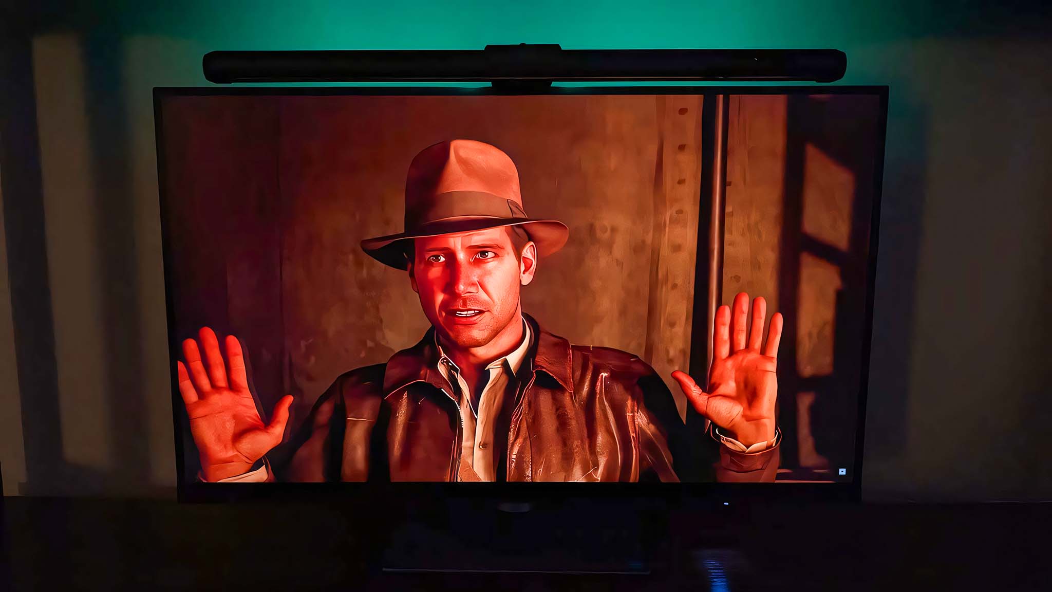 ASUS ROG Aura Monitor Light Bar on a monitor in midday, with faint teal RGB showing up on the wall behind the monitor. Indiana Jones and the Great Circle is on the screen.