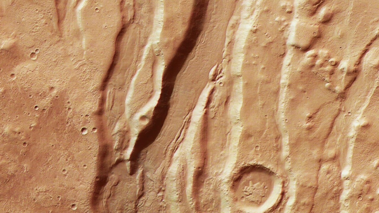 A close up of the surface of Mars, showing dramatic streaks and craters in its reddish brownish surface