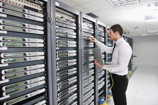 A man holding a laptop interacting with a rack of servers
