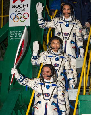 Russian cosmonaut Mikhail Tyurin, Expedition 38 Soyuz commander, holds the Olympic torch as Flight Engineer Koichi Wakata of Japan and Rick Mastracchio of NASA (top) wave farewell prior to boarding the Soyuz TMA-11M rocket for launch, Thursday, Nov. 7, 20