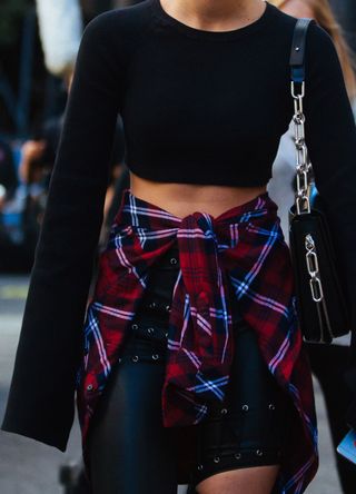 American Victoria's Secret Angel model Taylor Hill wears reflective sunglasses, a long-sleeve cropped black top, a black chain purse, a red plaid shirt around her waist, and black pants after the Marc Jacobs show at Hammerstein Ballroom on September 15, 2016 in New York City.