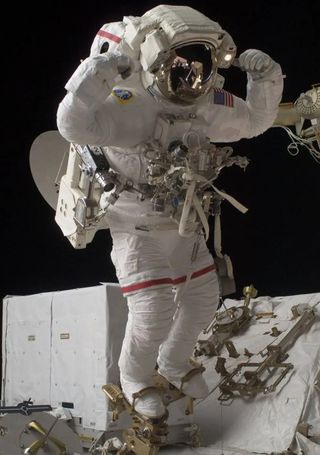 astronaut in a spacesuit with their feet in foot restraints. the astronaut raises his hands above his head