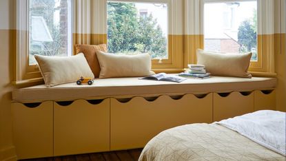 A children's bedroom painted in yellow with window seat storage