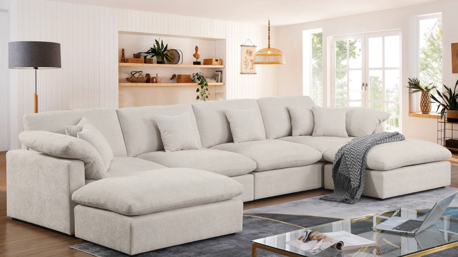 a living room with a large sectional, a gray rug, a coffee table, and a set of built-in shelves behind the couch