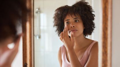 morning skincare routine - woman applying face cream in the mirror - gettyimages-1464166549