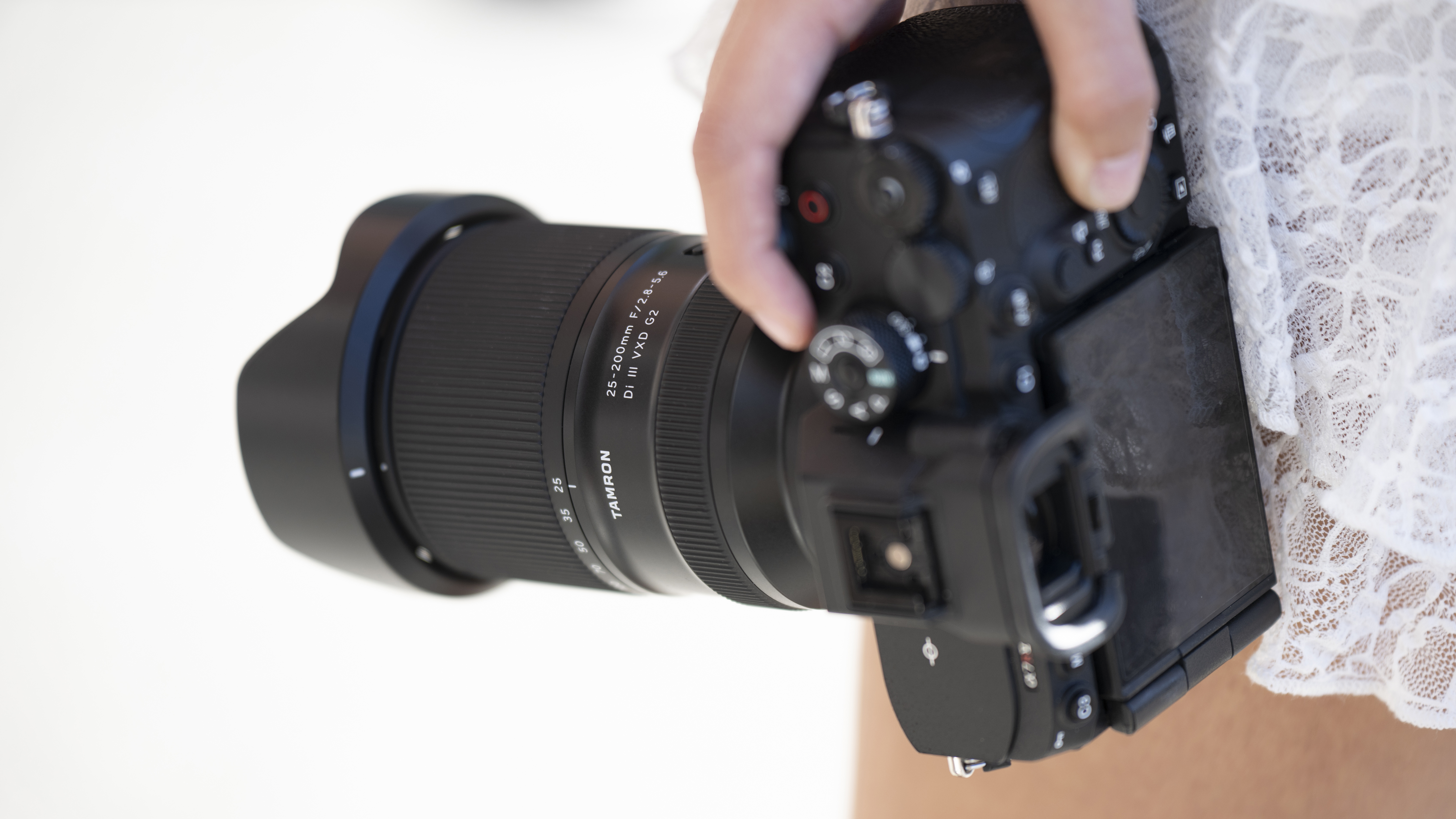 The Tamron 25-200mm f/2.8-5.6 DI III VXD G2 in a person's hand mounted on a camera