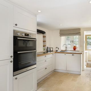 Cotswold stone cottage's white kitchen, with black oven and beige stone floor tiles