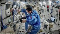 Two astronauts float in the busy white interior of a space station, holding equipment, wearing ppo masks.