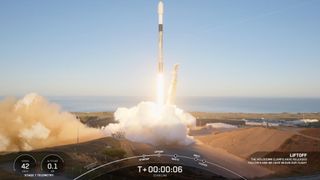 a black-and-white spacex falcon 9 rocket launches into a blue sky.