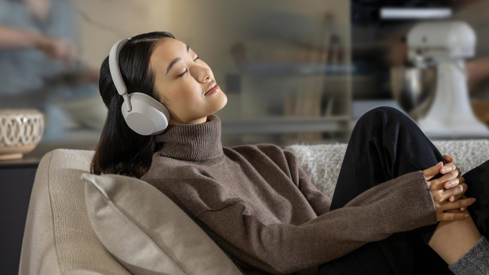 Woman on couch with Sony WH-1000XM5.