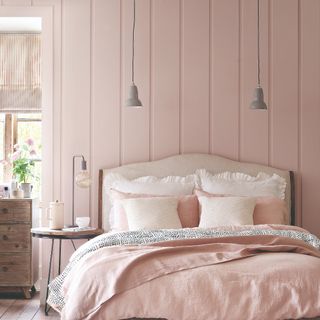 A pink bedroom with vertical wall panelling matching the linen bedding on the bed