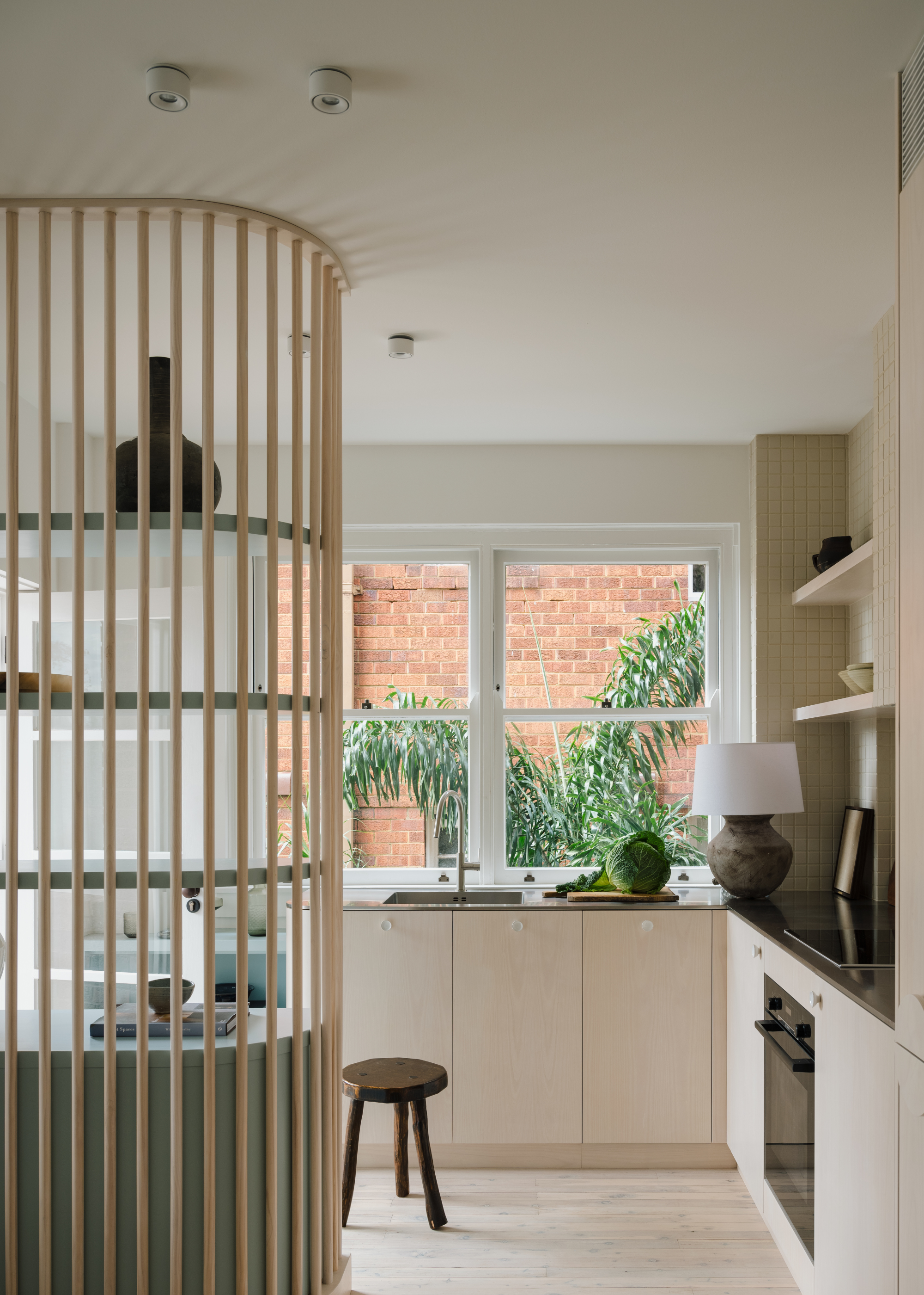 A small kitchen with a curved panelled display wall, a small stool and a lamp