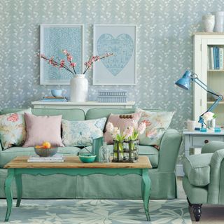 A duck egg living room with patterned wallpaper, a green sofa and wall art