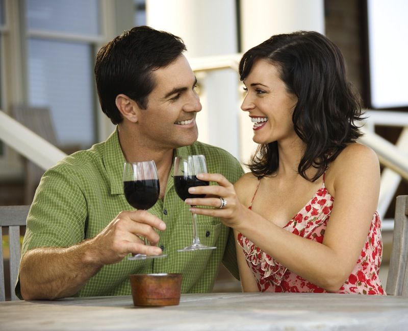 A couple toast with glasses of red wine.