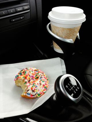 coffee in car drinks holder and donut on a napkin near gear stick