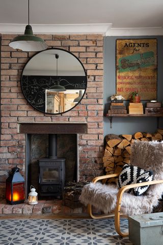A cozy rocking armchair in front of fireplace with exposed brick, and a grey and white rug and round mirror