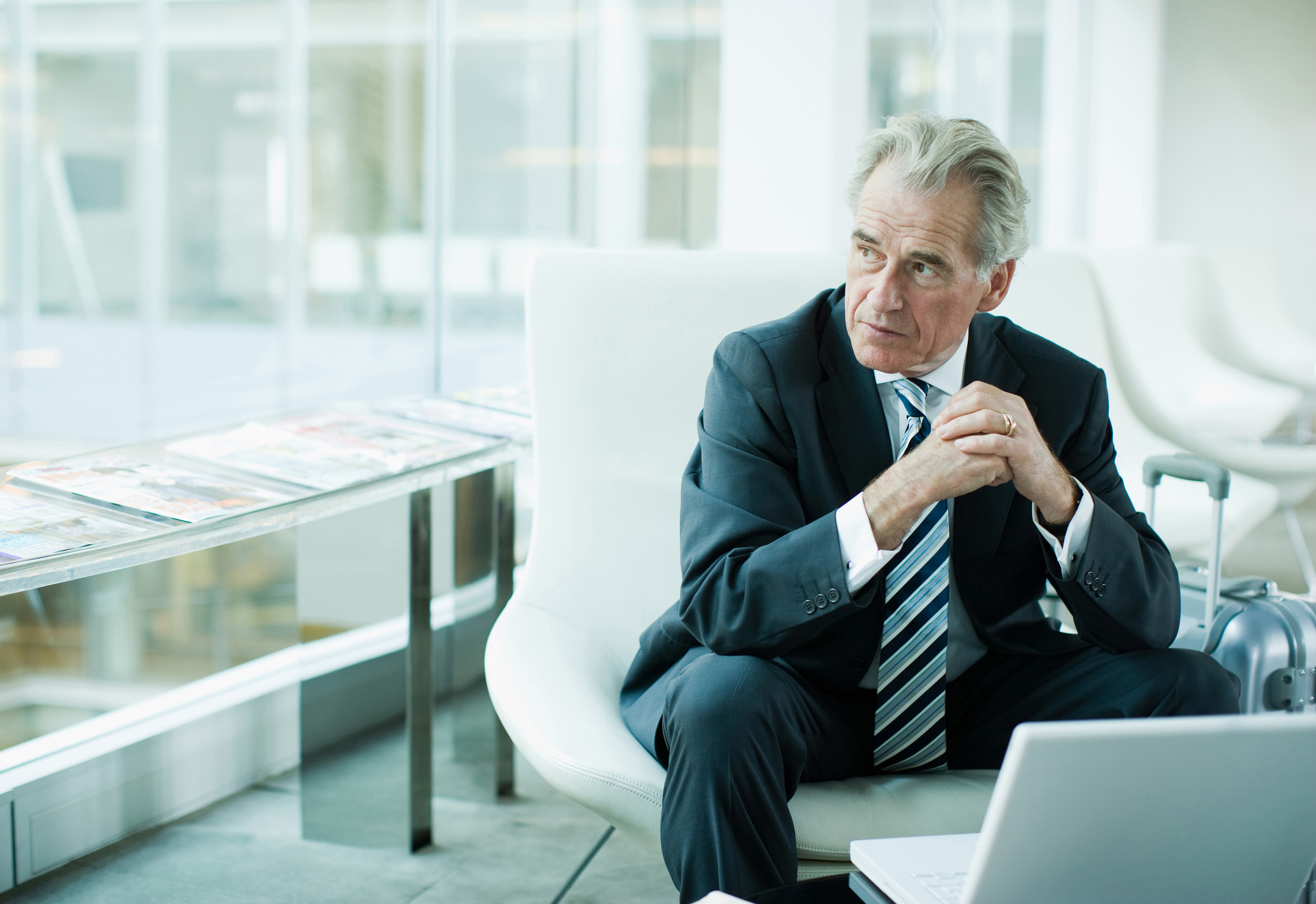 An older business man in a suit and tie sits in front of a laptop and looks to the side. He appears thoughtful or impatient.