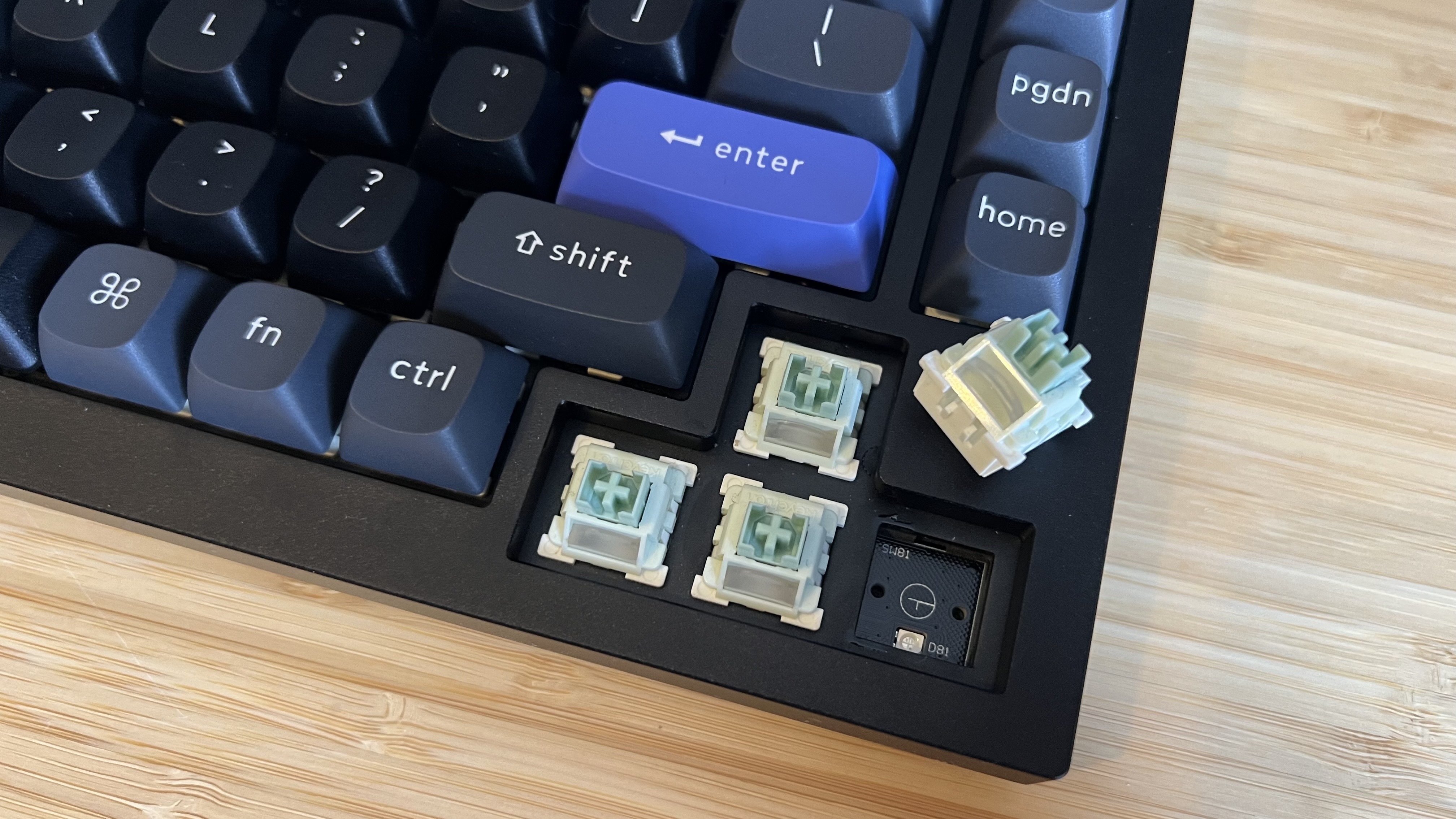 Keychron Q1 HE 8K gaming keyboard with arrow key caps removed, showing magnetic switches with one taken out of the PCB
