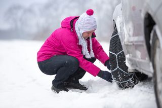 woman in pink attaching snow chains to car wheels