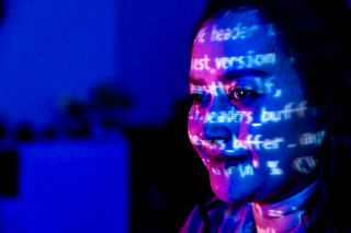 A woman staring at code in a room lit in blue and purple