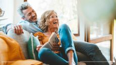 Man and woman sitting on the sofa, woman with book, smiling and laughing