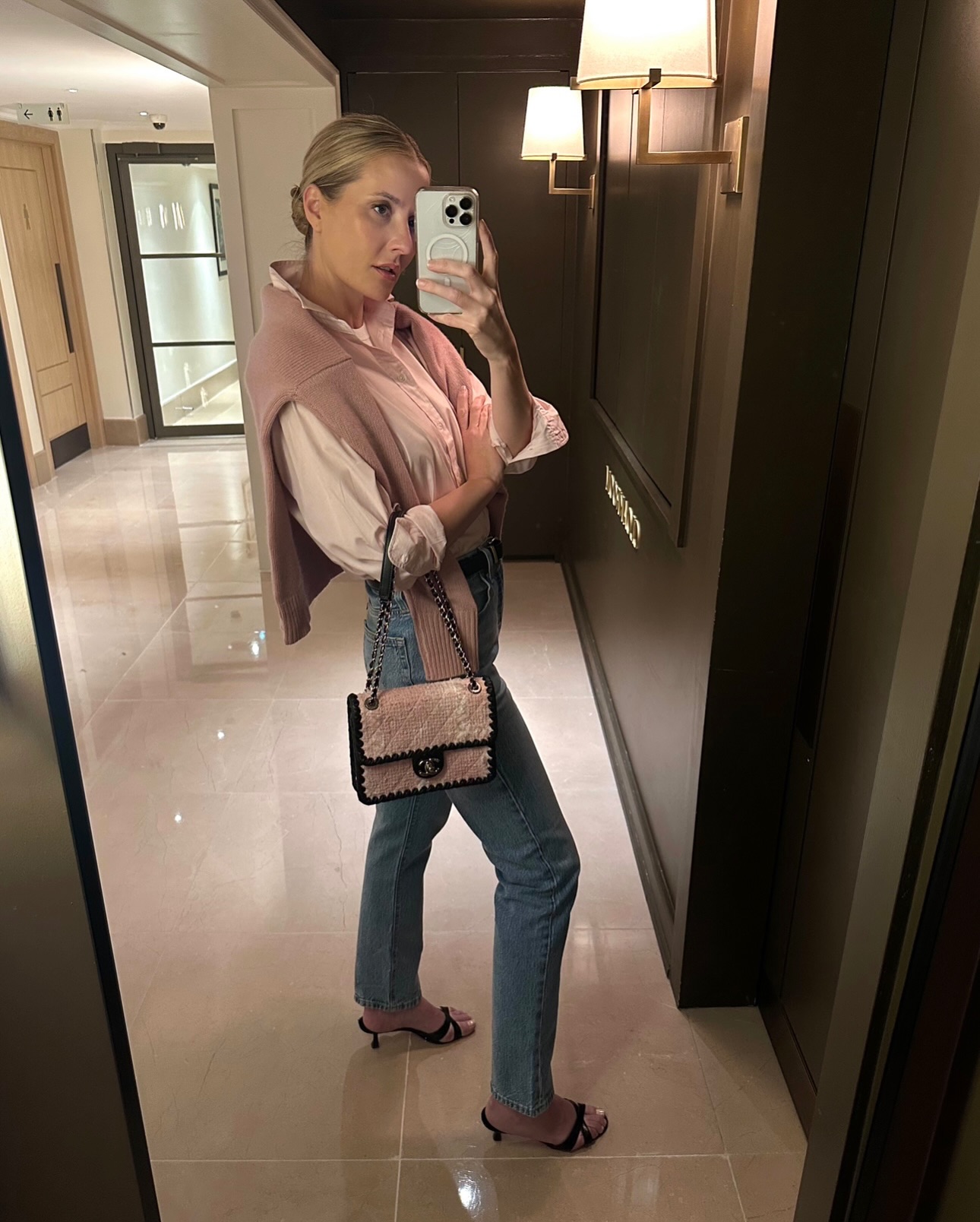 A woman wears skinny jeans with a pink poplin shirt and matching sweater