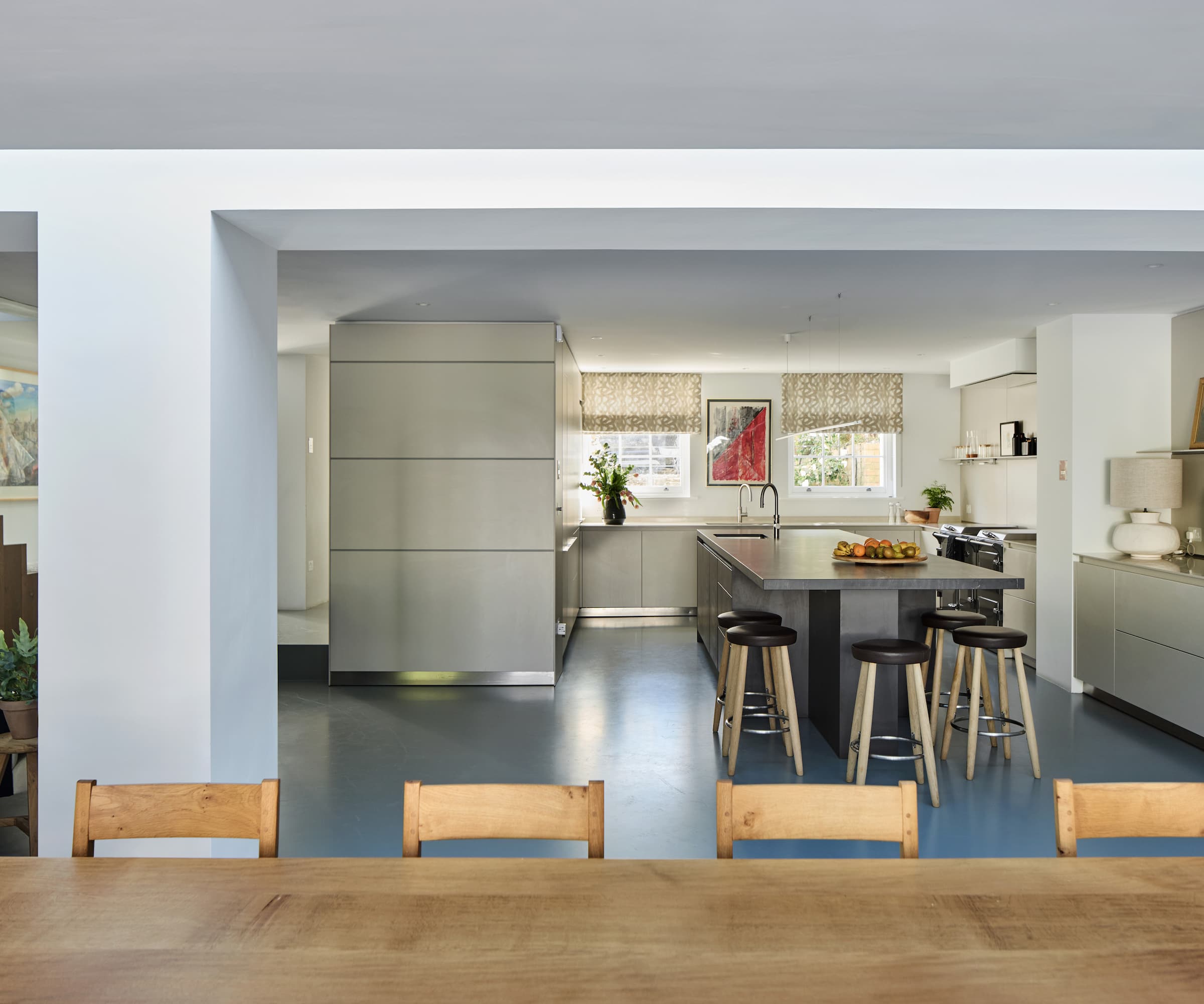 A kitchen dining area with a long wooden table and grey kitchen island surrounded by white cabinets