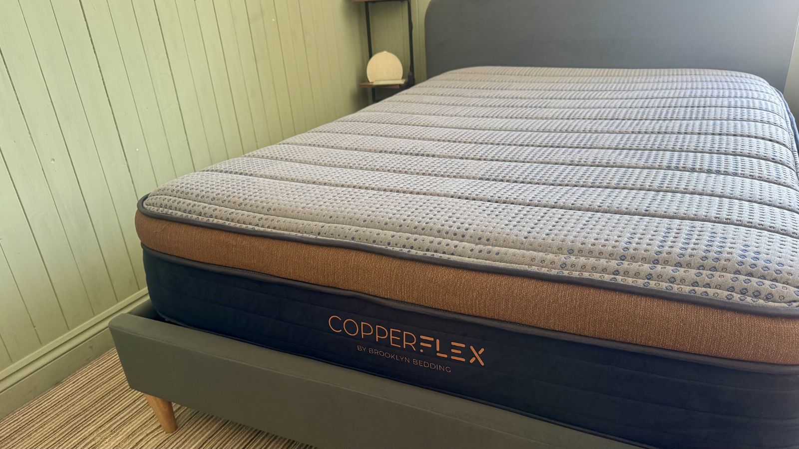 Grey, navy and bronze Brooklyn Bedding Copperflex Mattress on grey bed frame in bedroom with panelled walls