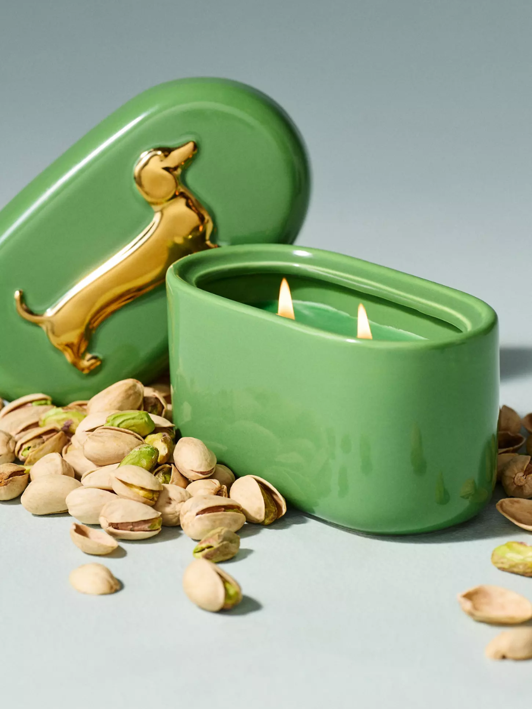 A green ceramic pistachio candle with a gold-embossed dachshund lid