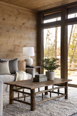 cream sofa next to window with wooden walls rustic coffee table and views of trees neutral furnishings