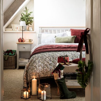 guest bedroom dressed for christmas with double bed with grey frame and matching bedside table with lamp white bedlinen and a green and red throw