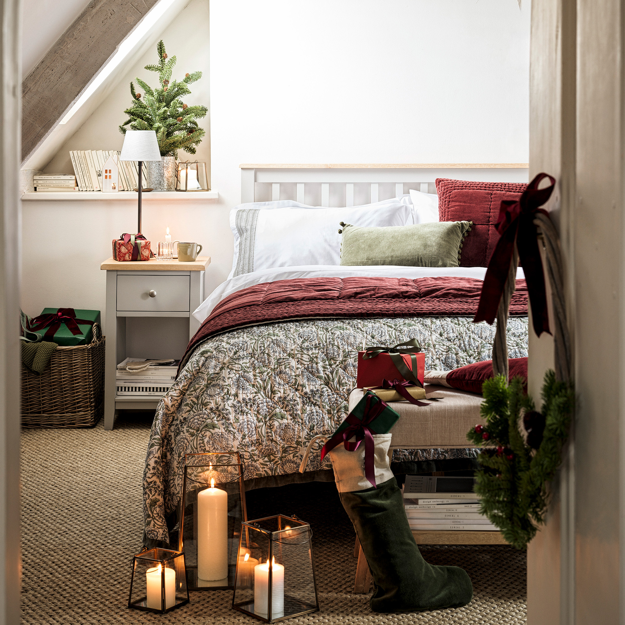 guest bedroom dressed for christmas with double bed with grey frame and matching bedside table with lamp white bedlinen and a green and red throw